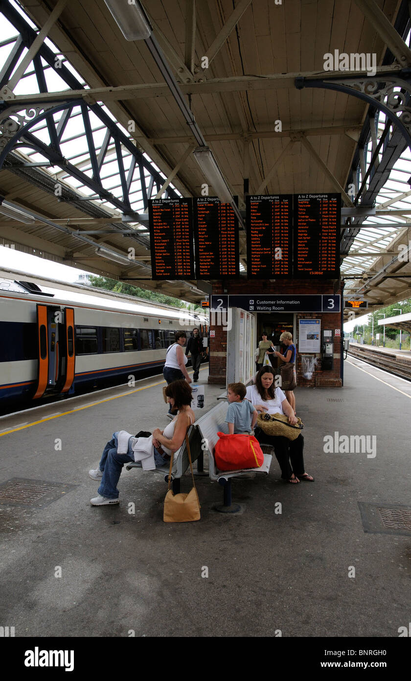 Passagiere kommen und warten auf einen Zug unterhalb der Anzeigentafel Informationen auf Basingstoke Bahnhof in Hampshire Stockfoto