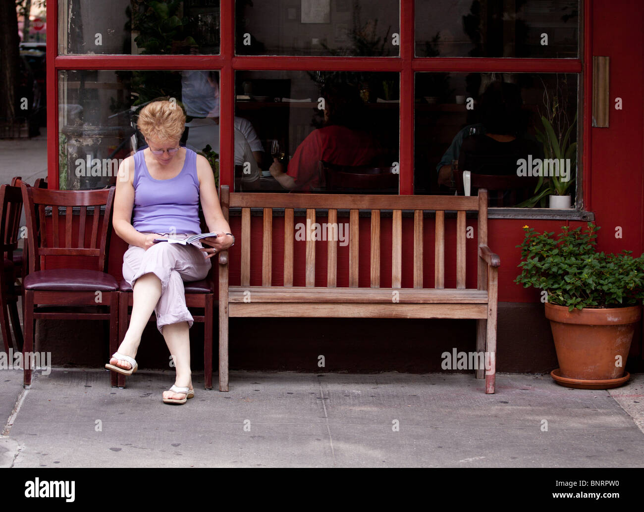 Eine Frau auf einem Stuhl außerhalb ein Cafe auf einer Straße der Stadt in Greenwich Village, Manhattan, New York, USA sitzen Stockfoto