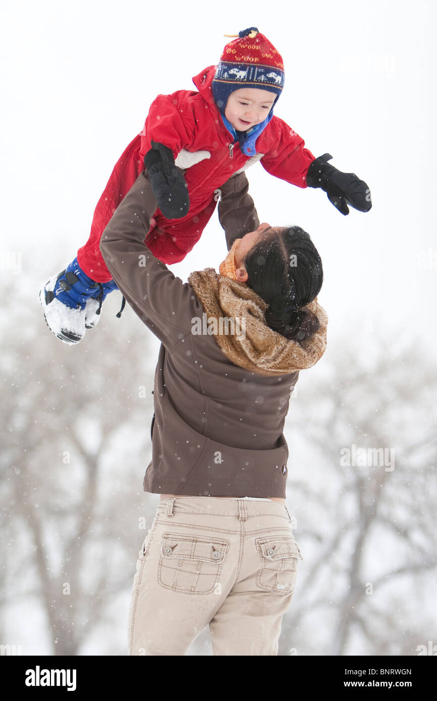 Ein zweier Jahre alter Junge spielt in einem schneebedeckten Feld während eines Schneesturms in einem roten Schneeanzug mit seiner Mutter in einem Park, Fort Collins, Colorado Stockfoto