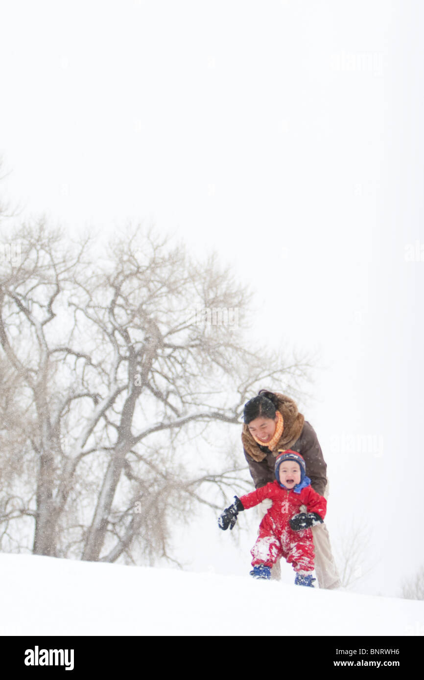 Ein zweier Jahre alter Junge spielt in einem schneebedeckten Feld während eines Schneesturms in einem roten Schneeanzug mit seiner Mutter in einem Park, Fort Collins, Colorado Stockfoto