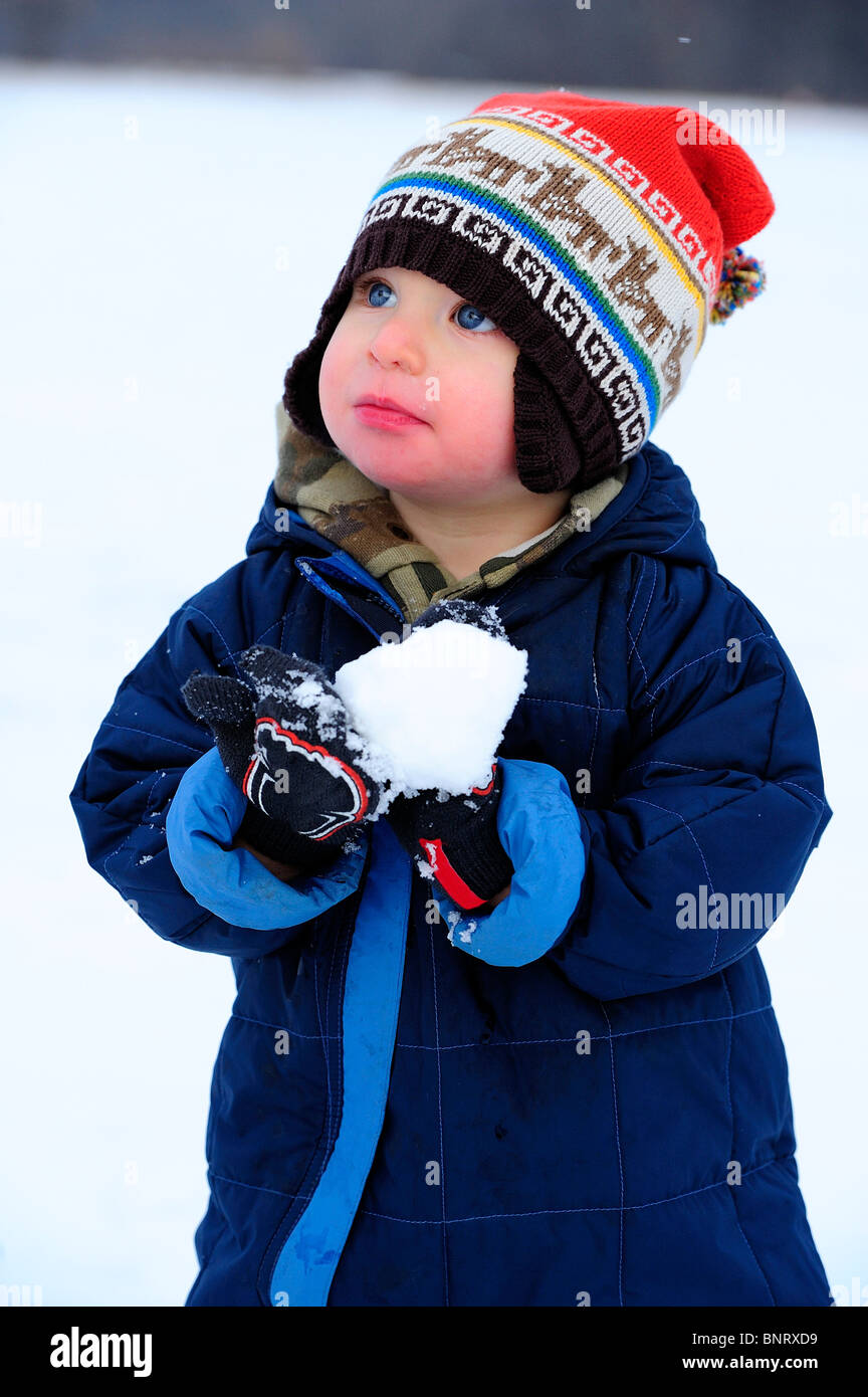 Kleinkind spielt mit Schnee in einem Schneeanzug. Stockfoto