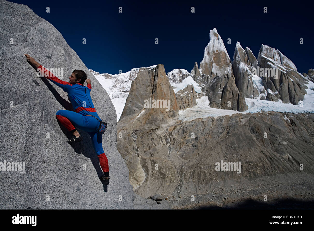 Mann im Anzug Spiderman klettert vor Berg. Stockfoto