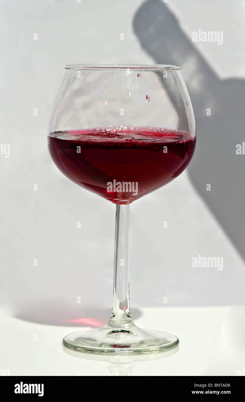 Dieses Bild hat eine lange stemmed Weinglas mit Rotwein gegossen und einen Schatten einer Weinflasche aus auf die Seite. Stockfoto
