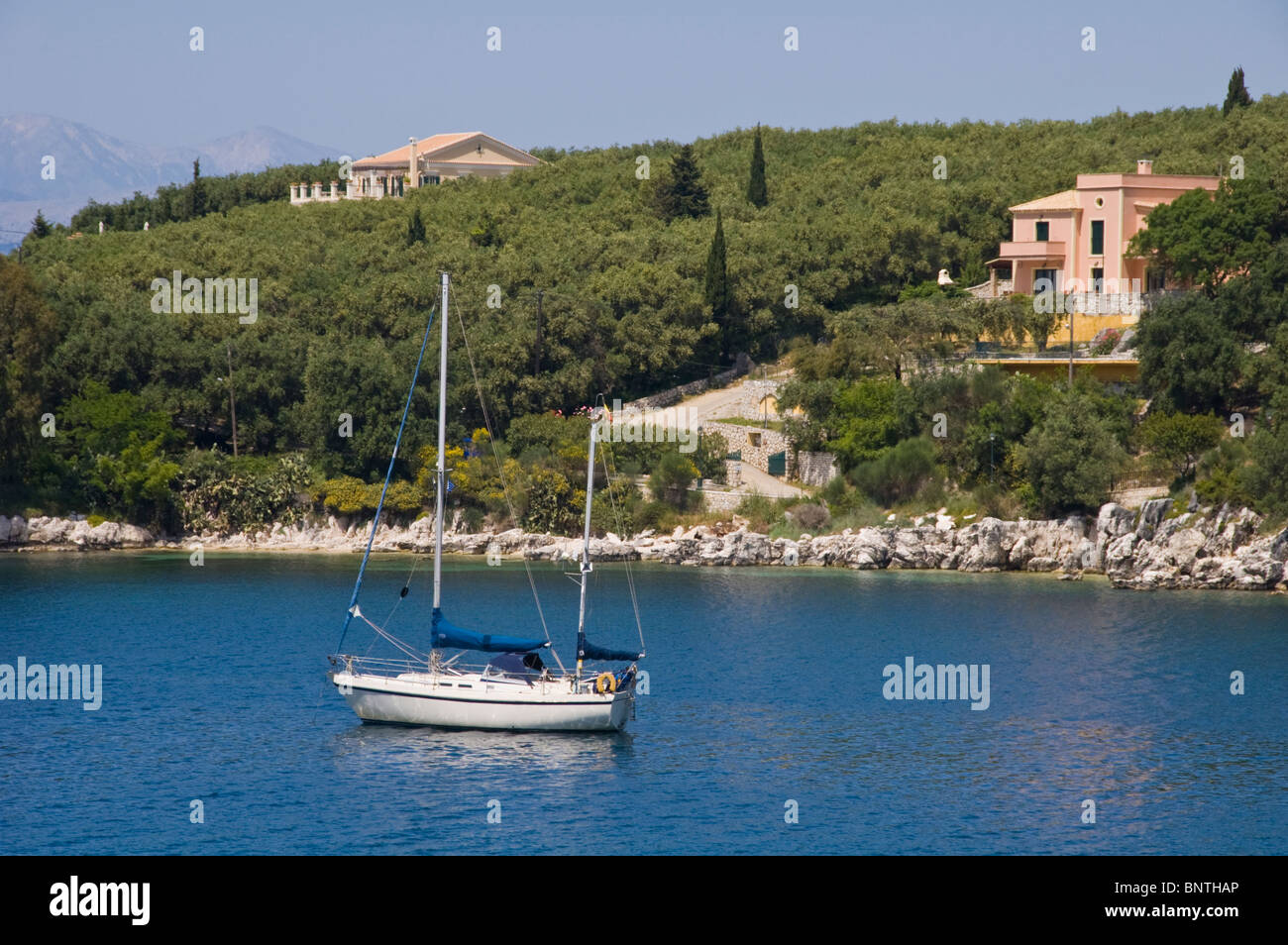 Luxus-Villen am bewaldeten Hang mit Segelyacht vor Anker in der Bucht bei Kassiopi auf der griechischen Mittelmeer Insel Korfu Griechenland Stockfoto