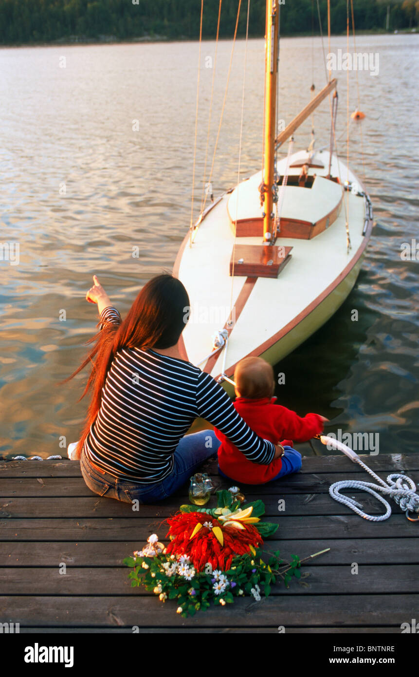 Mutter und Kind sitzt auf hölzerne dock mit Ankern Segelboot und Teller mit Flusskrebsen, Kerzen und Aquavit in Schweden Stockfoto