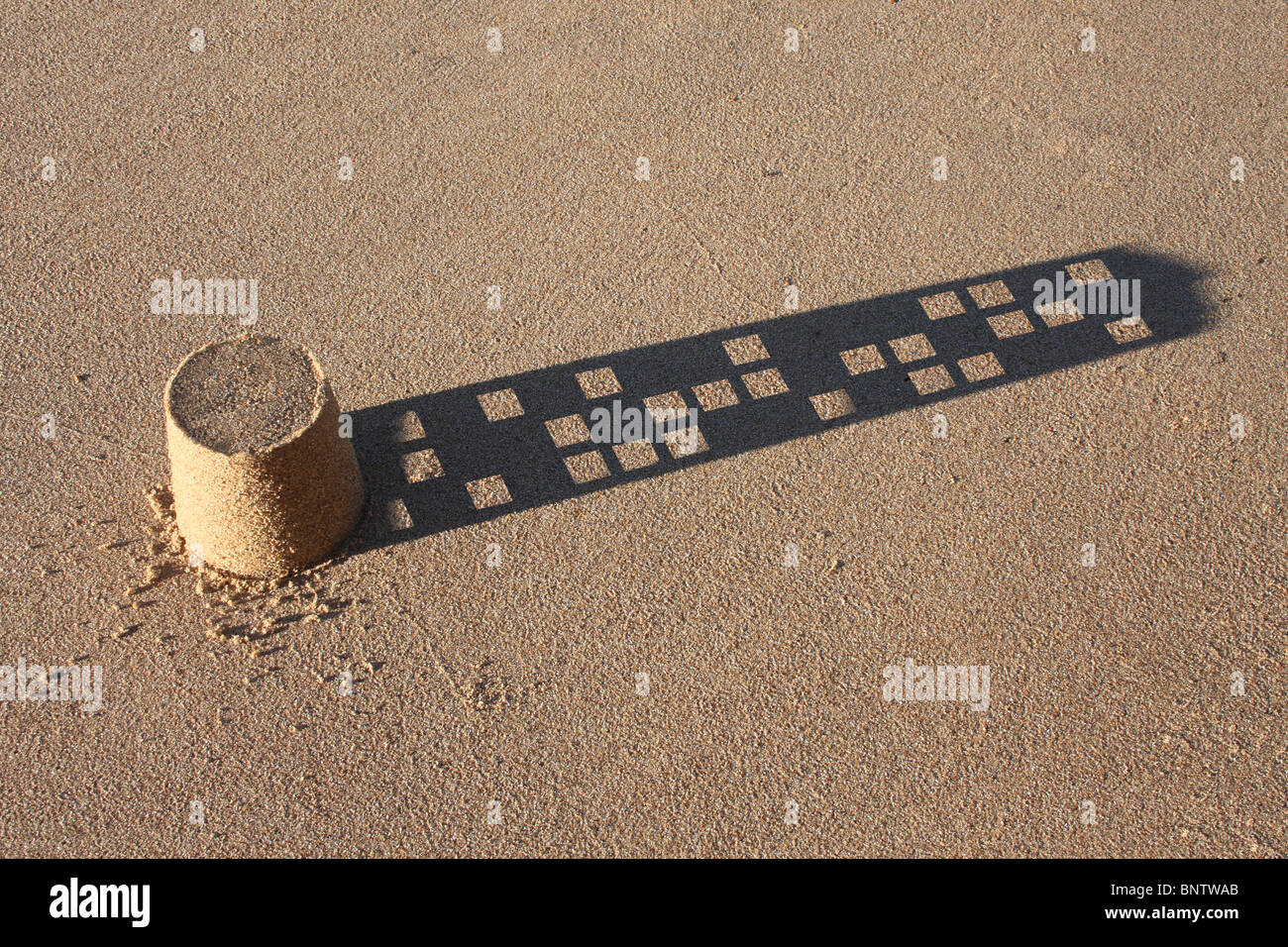 Eine kleine Sandburg mit einem Wolkenkratzer eines Schattens. Stockfoto