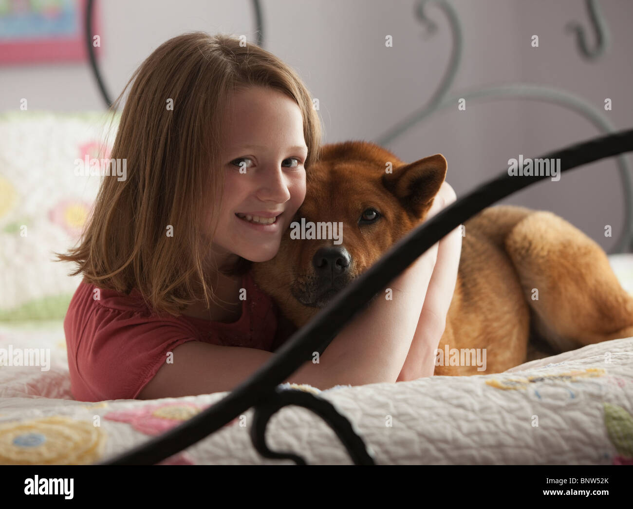 Junges Mädchen umarmt Hund auf Bett Stockfoto