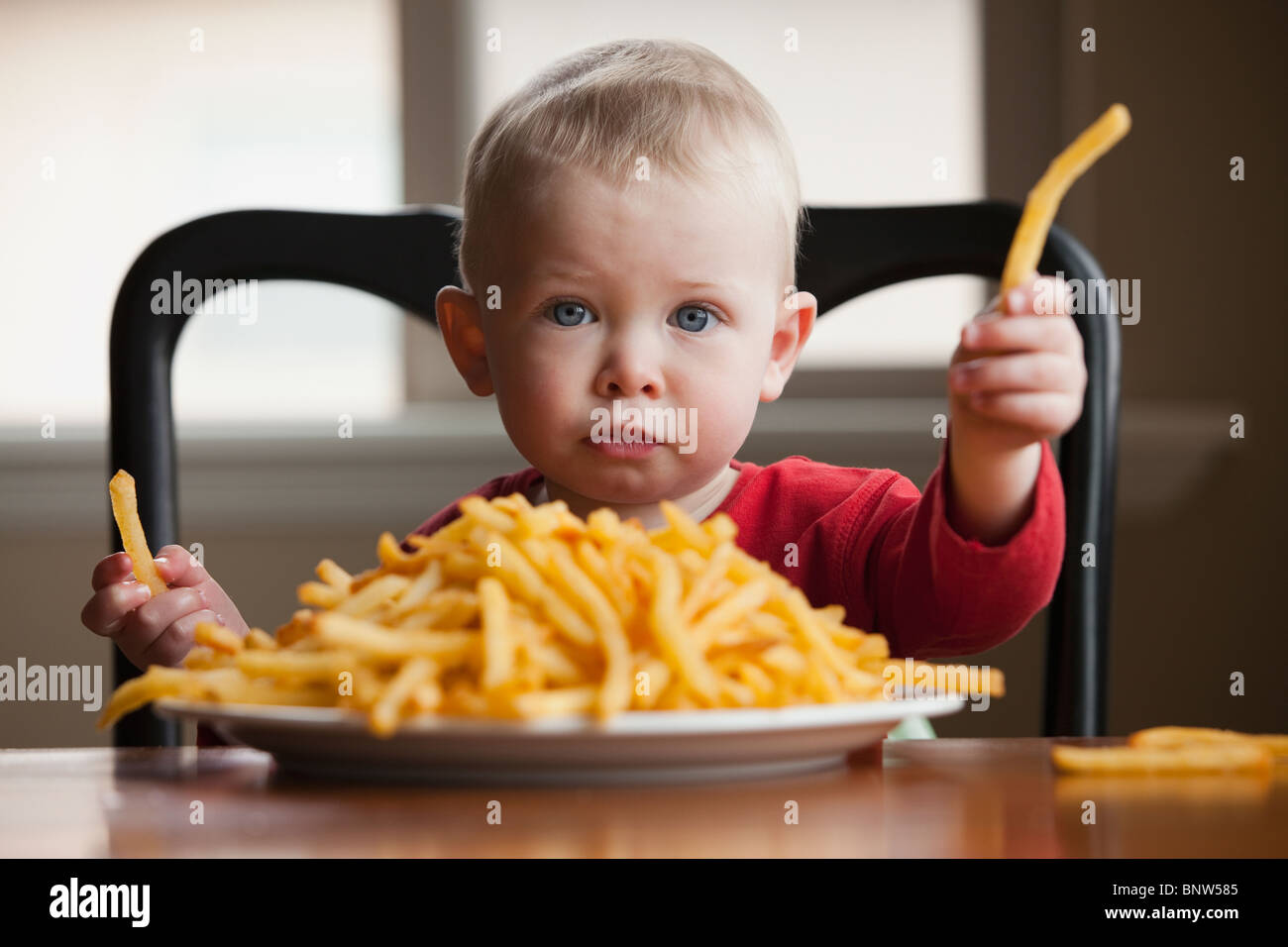 Kleinkind Essen einen großen Teller mit Pommes frites Stockfoto