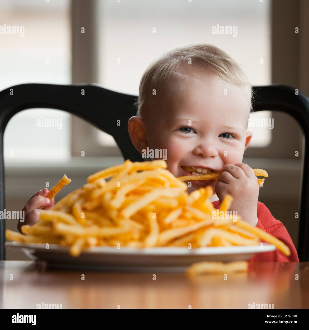 Kleinkind Essen einen großen Teller mit Pommes frites Stockfoto