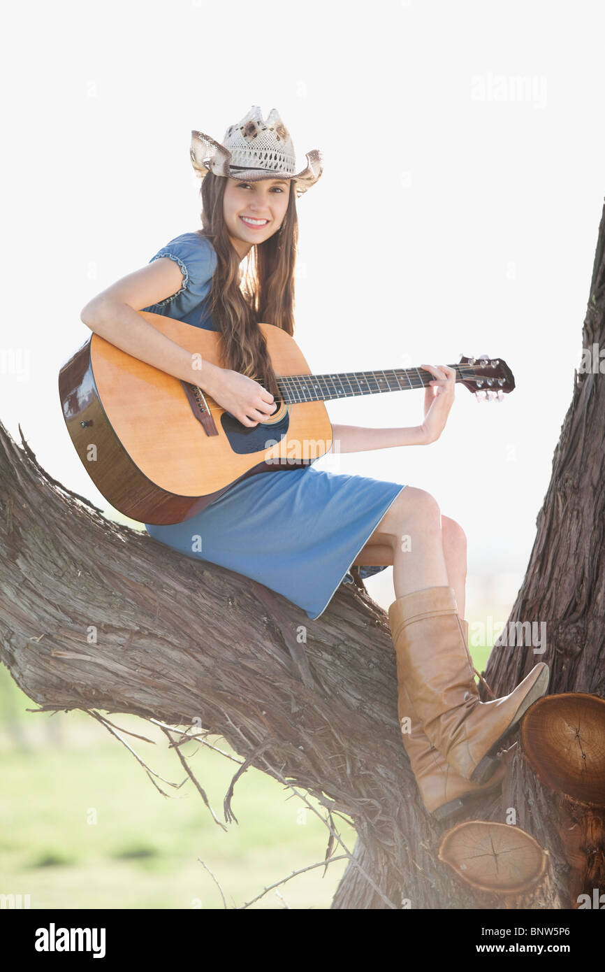 Cowgirl sitzt im Baum, Gitarre spielen Stockfoto