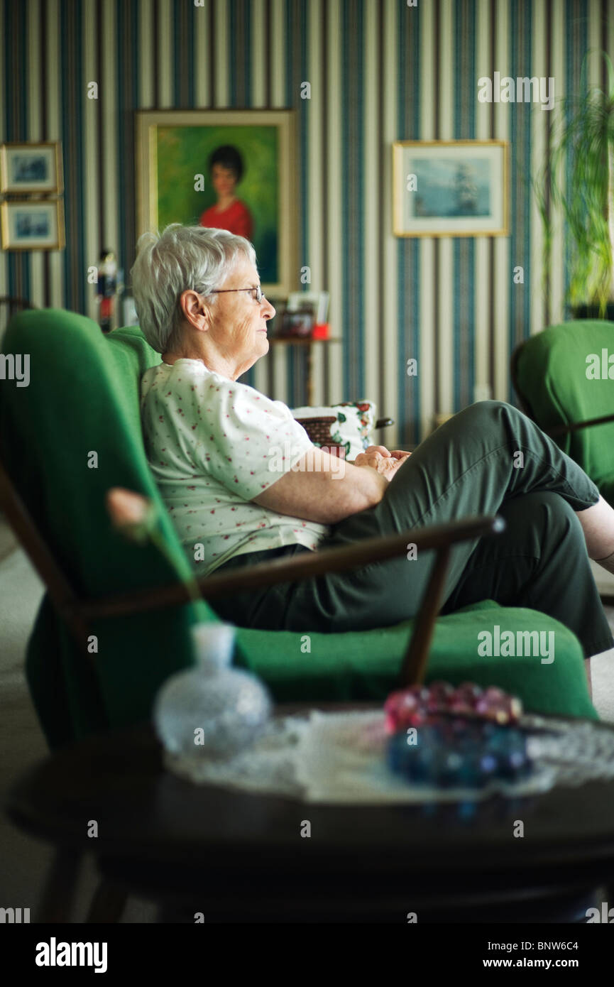 Alte Frau im Profil sitzt auf der Couch im Wohnzimmer. Stockfoto
