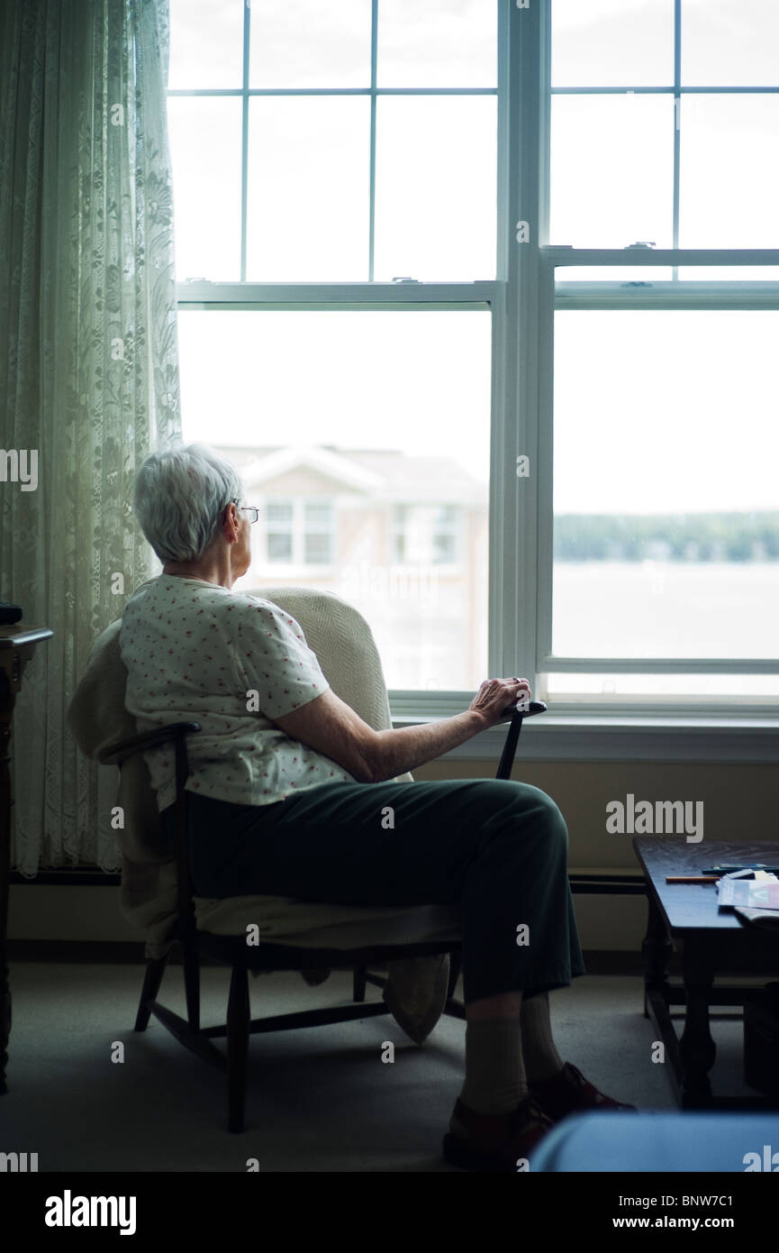 Alte Frau im Wohnzimmer Stuhl schaut aus Fenster. Stockfoto