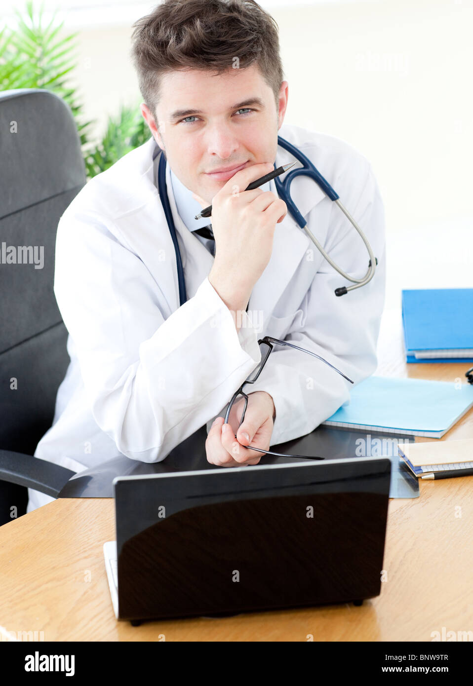 Lächelnd männlichen Arzt mit einem Laptop sitzt an seinem Schreibtisch Stockfoto