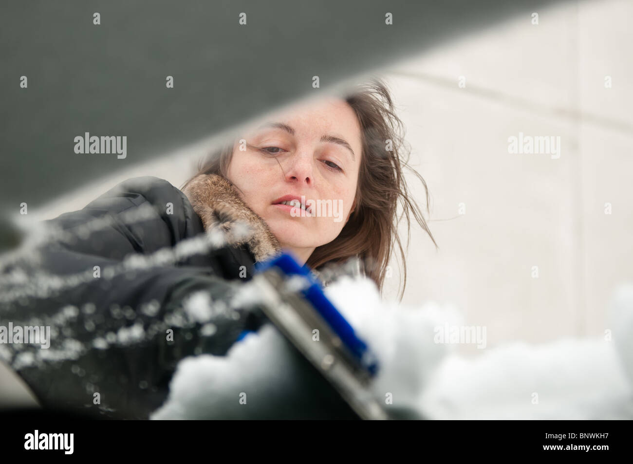 Junge Frau, die Reinigung der Autoscheiben von Schnee in der Wintersaison Stockfoto