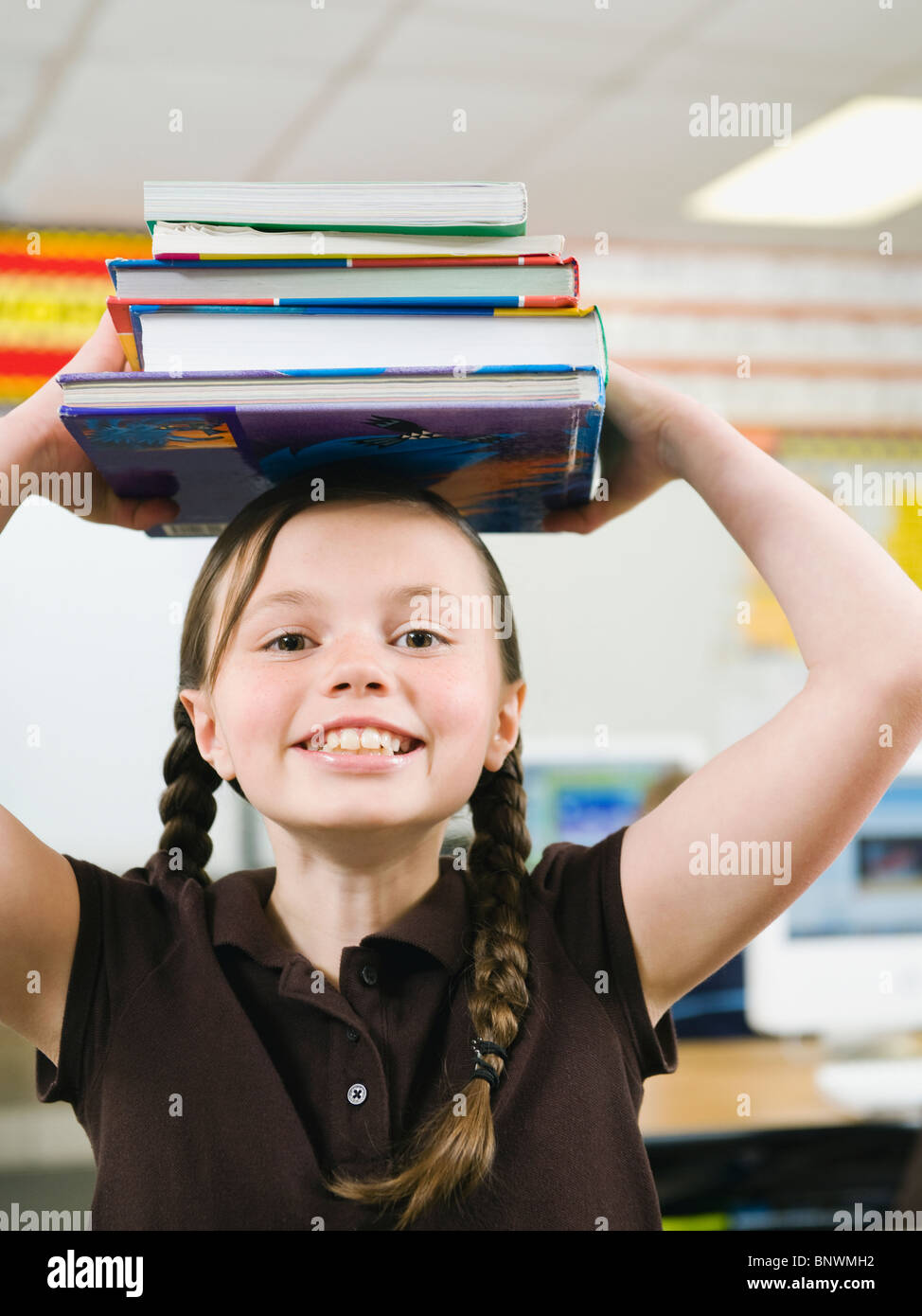 Elementare Student hält einen Stapel Bücher auf dem Kopf Stockfoto