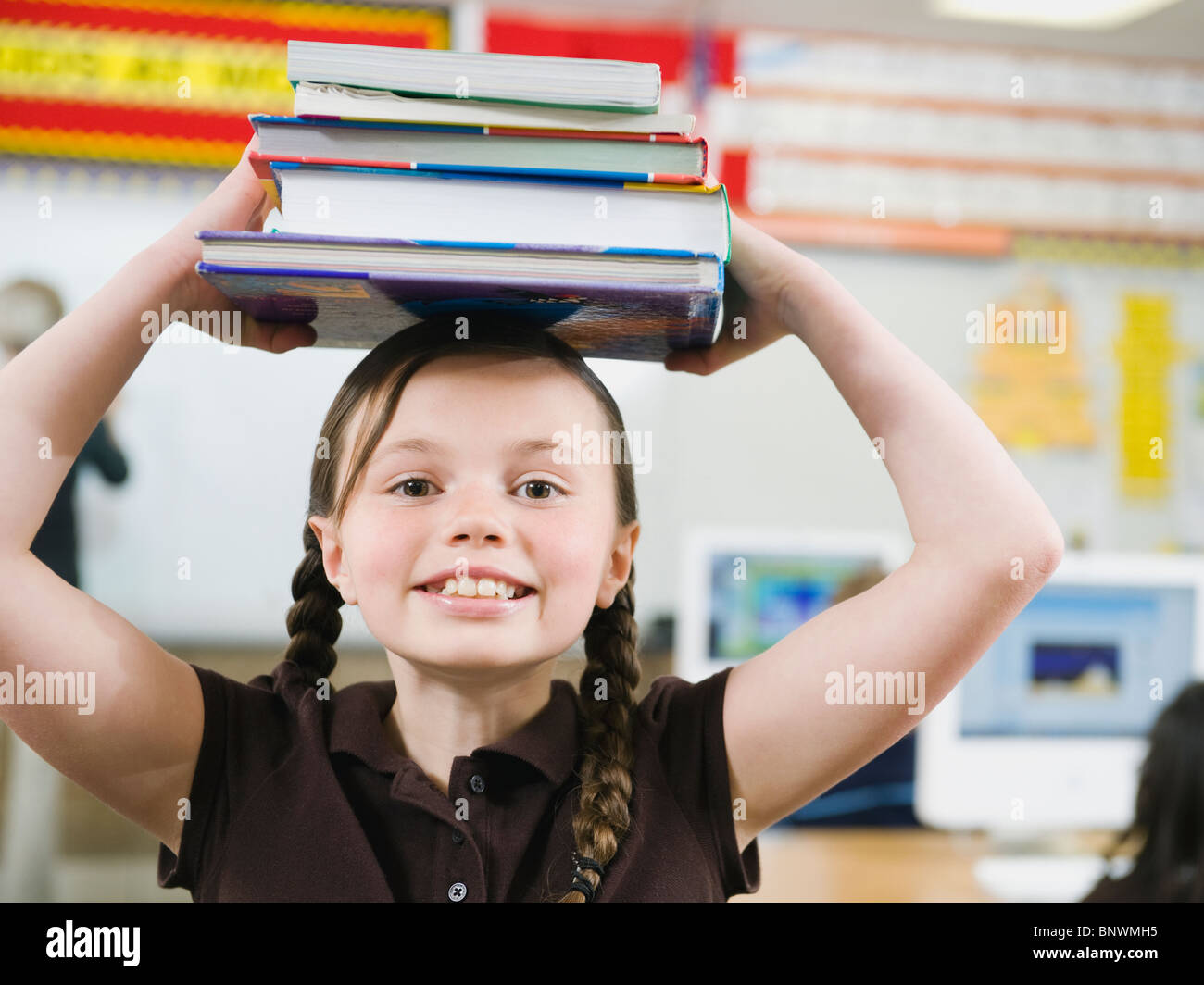 Elementare Student hält einen Stapel Bücher auf dem Kopf Stockfoto