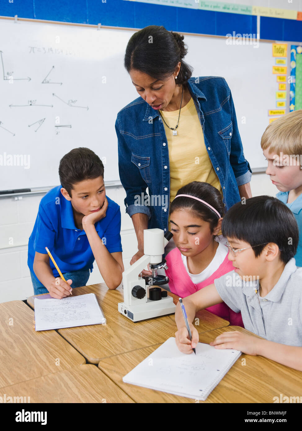 Lehrer und Grundschüler Mikroskop betrachten Stockfoto
