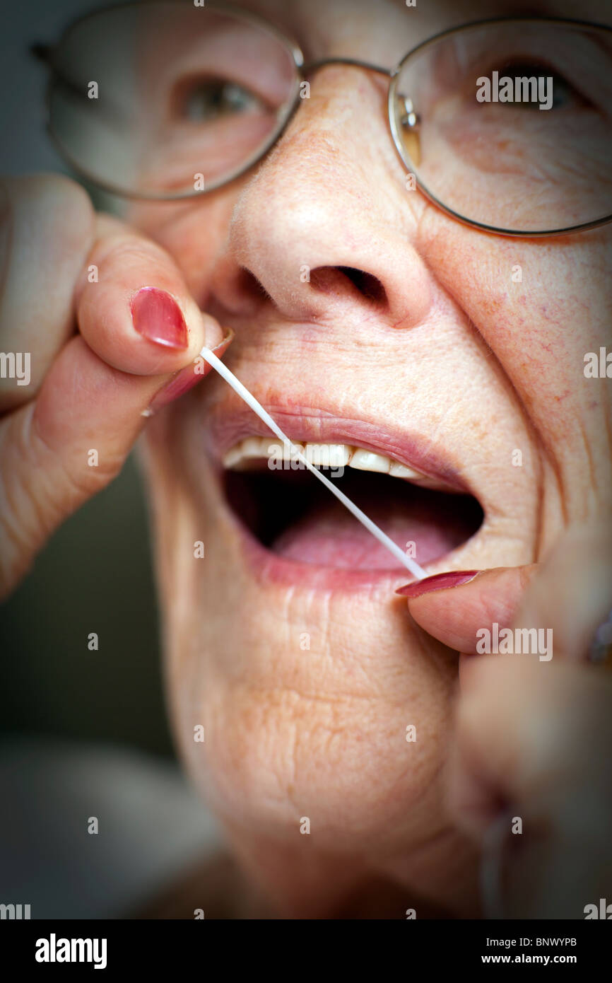 Eine ältere Dame nutzt Zahnseide um ihre Zähne zu reinigen und Zahnfleischerkrankungen vorzubeugen. Stockfoto