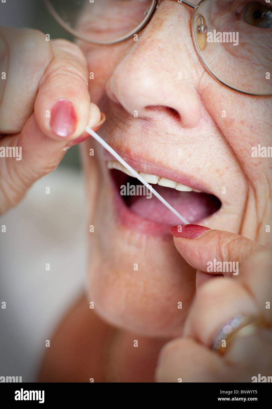 Eine ältere Dame nutzt Zahnseide um ihre Zähne zu reinigen und Zahnfleischerkrankungen vorzubeugen. Stockfoto