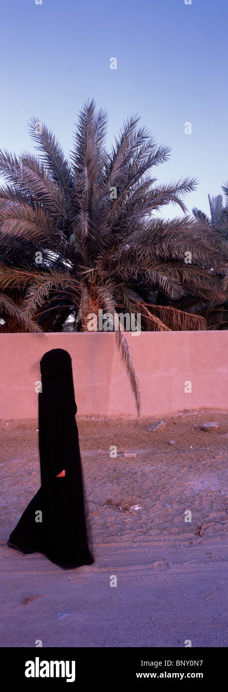 Panorama-Aufnahme der Trägerin traditionelle Abaya, vorbei an einer Wehrmauer befindet sich nahe Fort Fujairah, Fujairah, U.A.E. Stockfoto