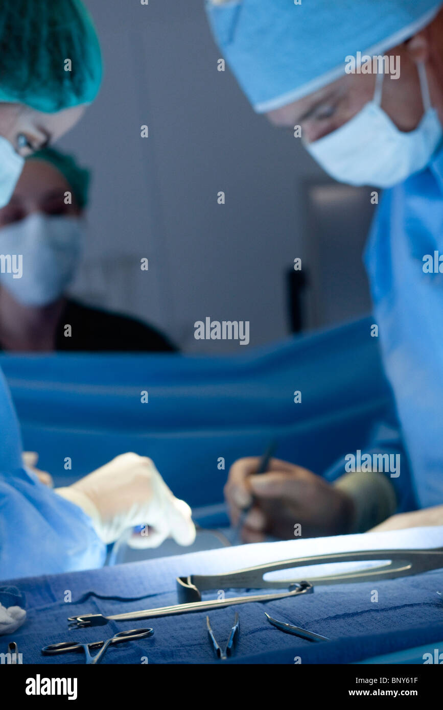 Chirurgische Instrumente, aufgereiht auf Tablett, Chirurgen, die im Hintergrund tätig Stockfoto