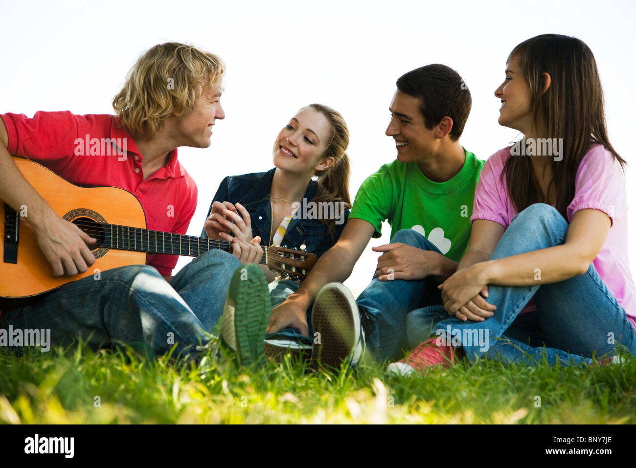 Junger Mann sitzt auf dem Rasen mit Freunden, spielt akustische Gitarre Stockfoto