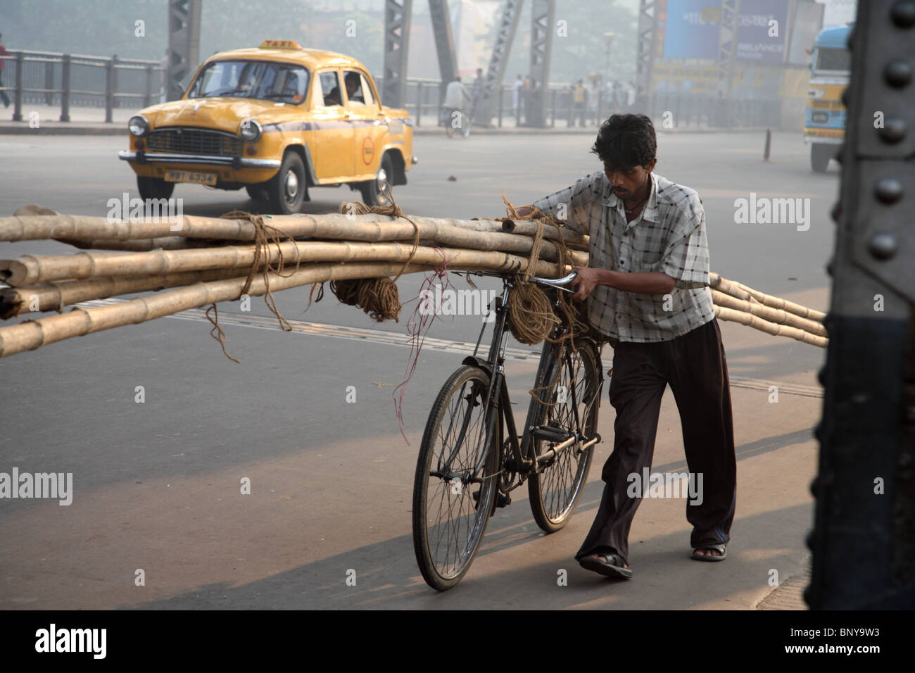 Ein Mann trägt eine Sammlung von Bambus Gerüststangen auf seinem Fahrrad über die massive Howrah Brücke in Kolkata, Indien. Stockfoto