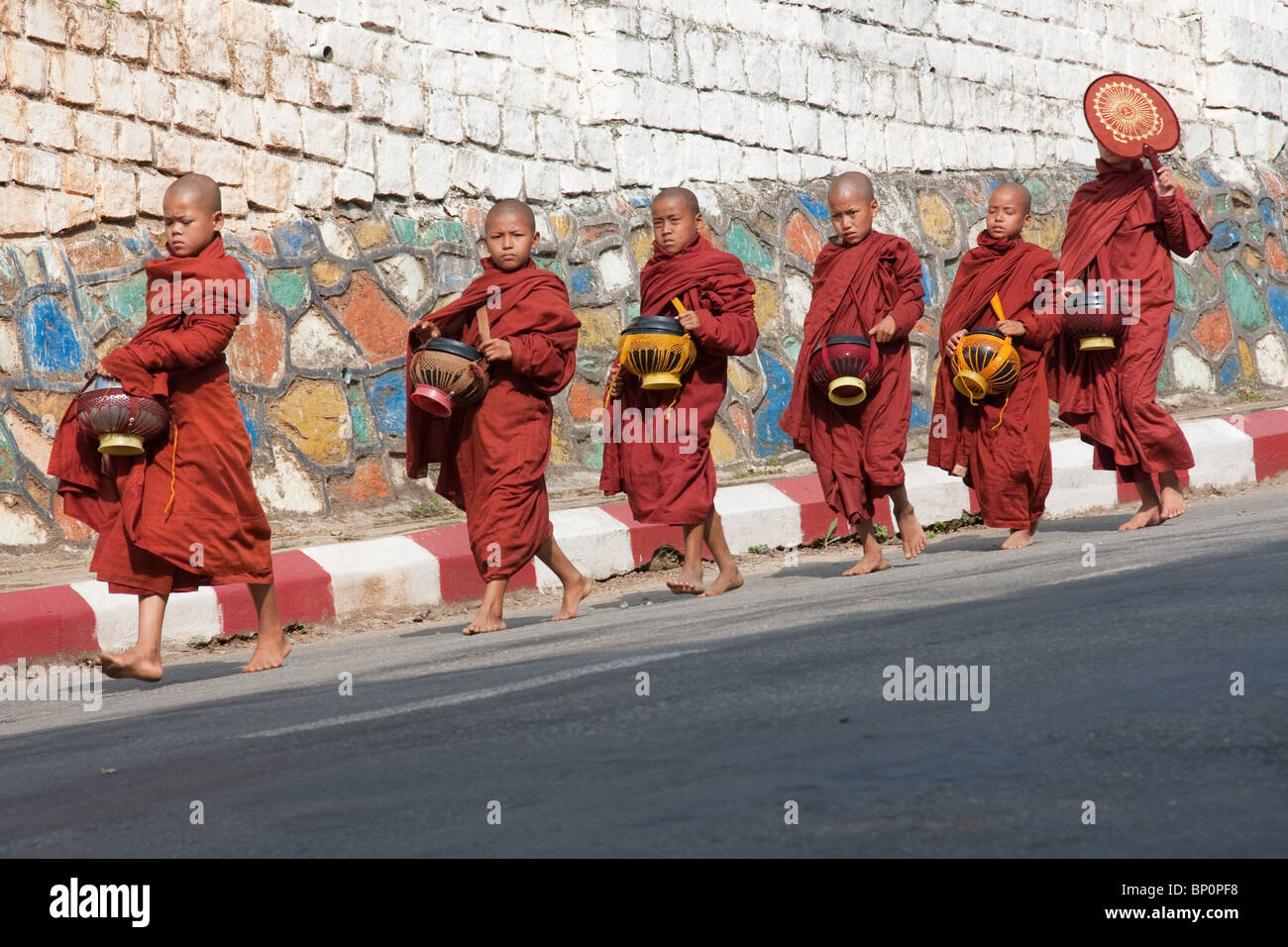 Novizen zu Fuß durch eine Mauer auf ihre tägliche Almosen Stockfoto