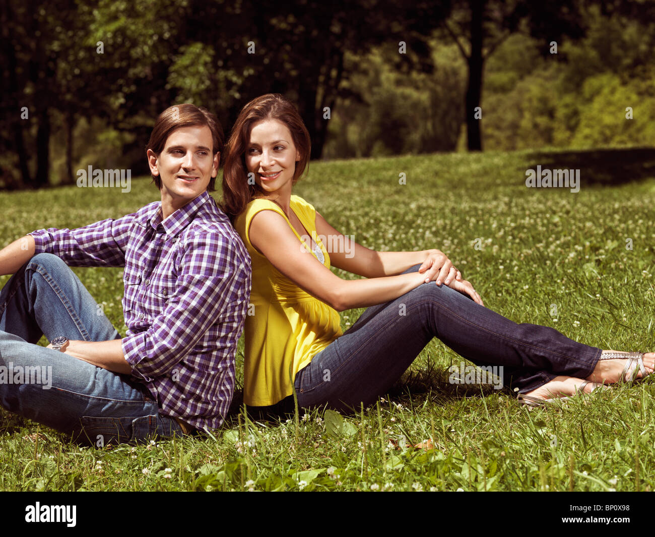 Lizenz erhältlich unter MaximImages.com - Junge glückliche, lächelnde Paare in ihren frühen 30ern, die auf Gras in einem Park sitzen Stockfoto