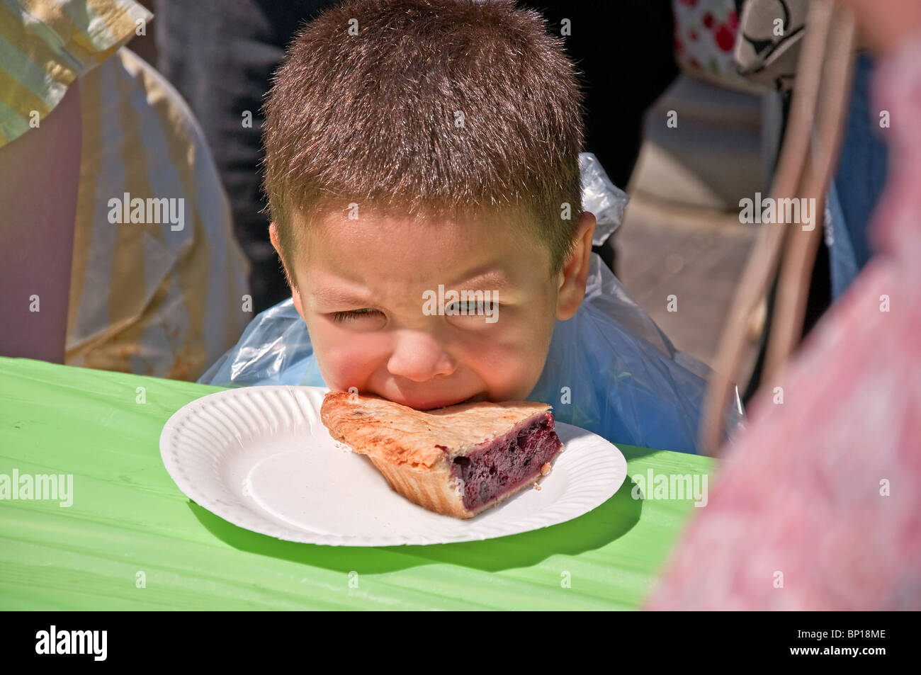Dieser süße 4 jährige Junge hat seinen Mund auf einem Stück Blaubeerkuchen während einer Kuchenwettessen. Er ist so jung und unsicher Stockfoto