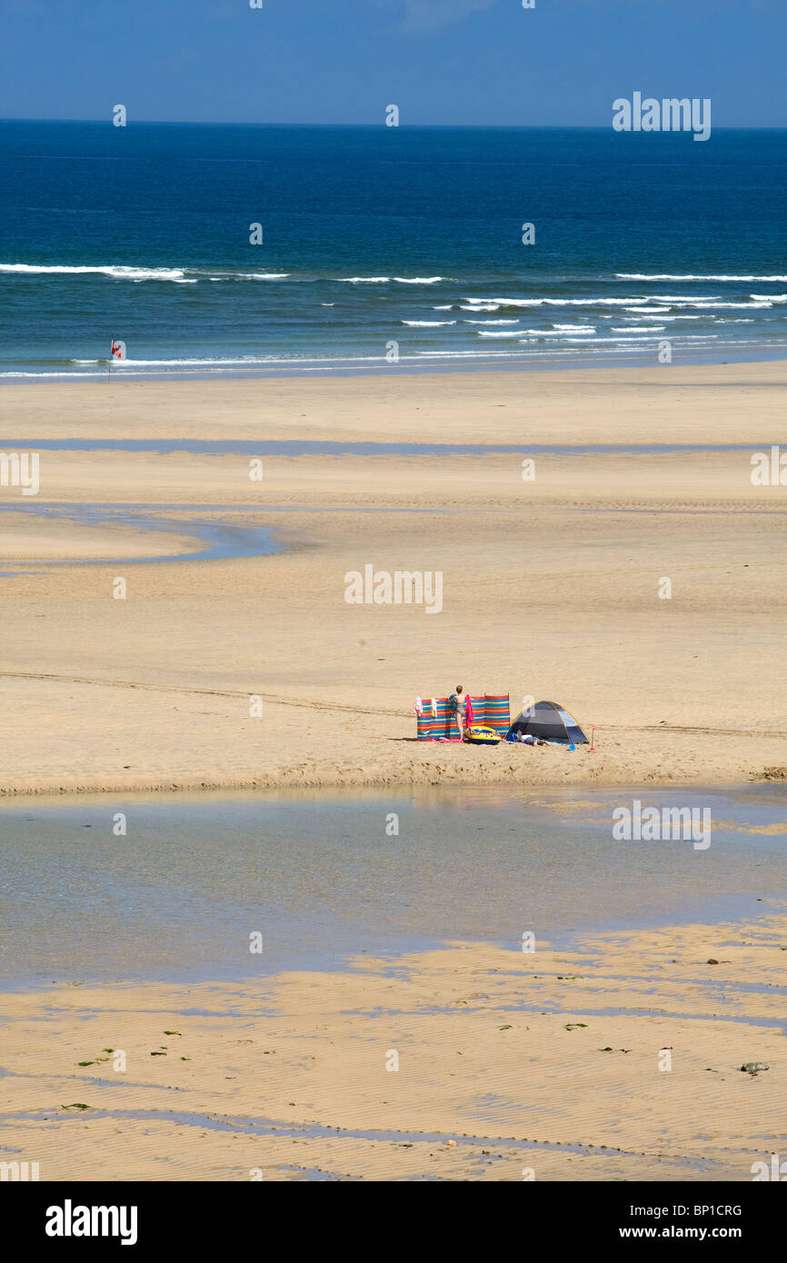 Eine einsame Figur mit Windschutz und kleines Zelt am Strand von Hayle, Cornwall Stockfoto