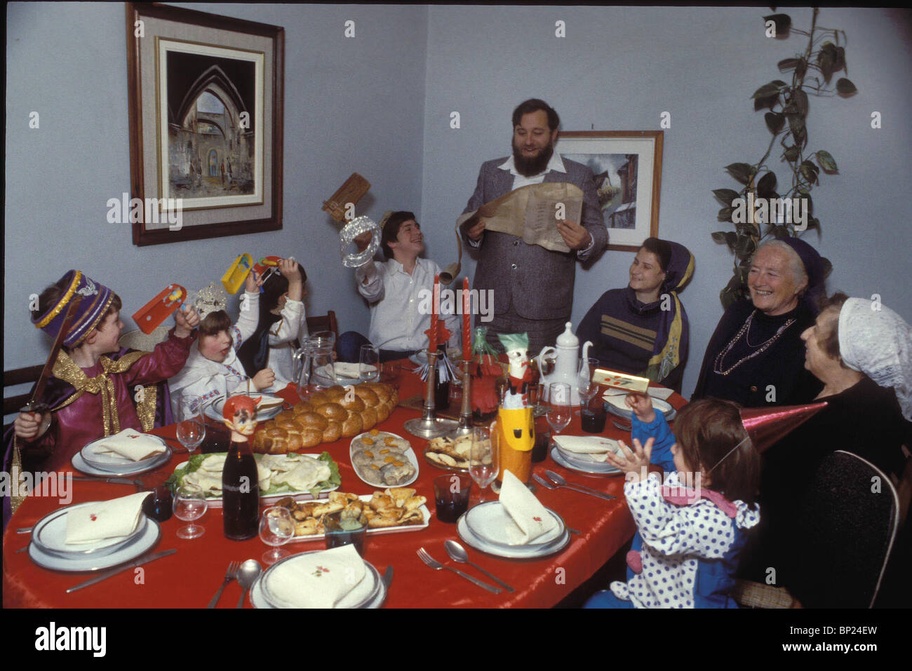 PURIM - JERUSALEM FAMILIE VERSAMMELTE DAS PURIM-FEST, WÄHREND DER VATER DER PURIM-SCHRIFTROLLE DIE KINDER VERWENDEN SPEZIELLE LIEST Stockfoto