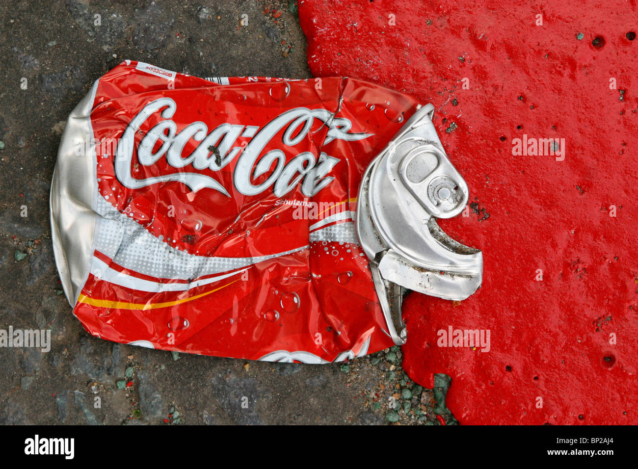 Eine Cola kann abgeflacht, in der Straße neben einem roten Route Straße Kennzeichnung in leuchtend rote Farbe, London, UK. Stockfoto