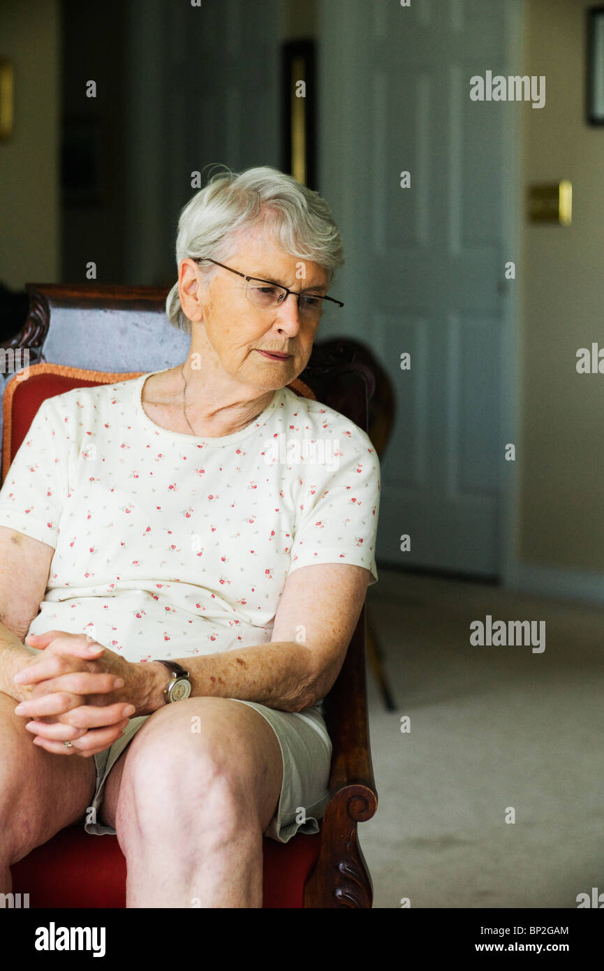 Unglücklich alte Frau sitzt im Wohnzimmer Stuhl wegsehen von Kamera. Stockfoto