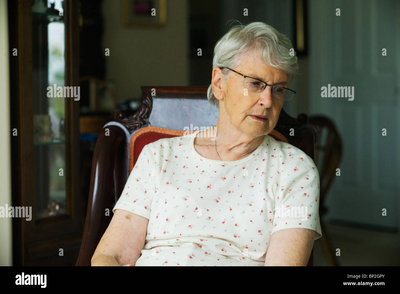 Unglücklich alte Frau sitzt im Wohnzimmer Stuhl wegsehen von Kamera. Stockfoto