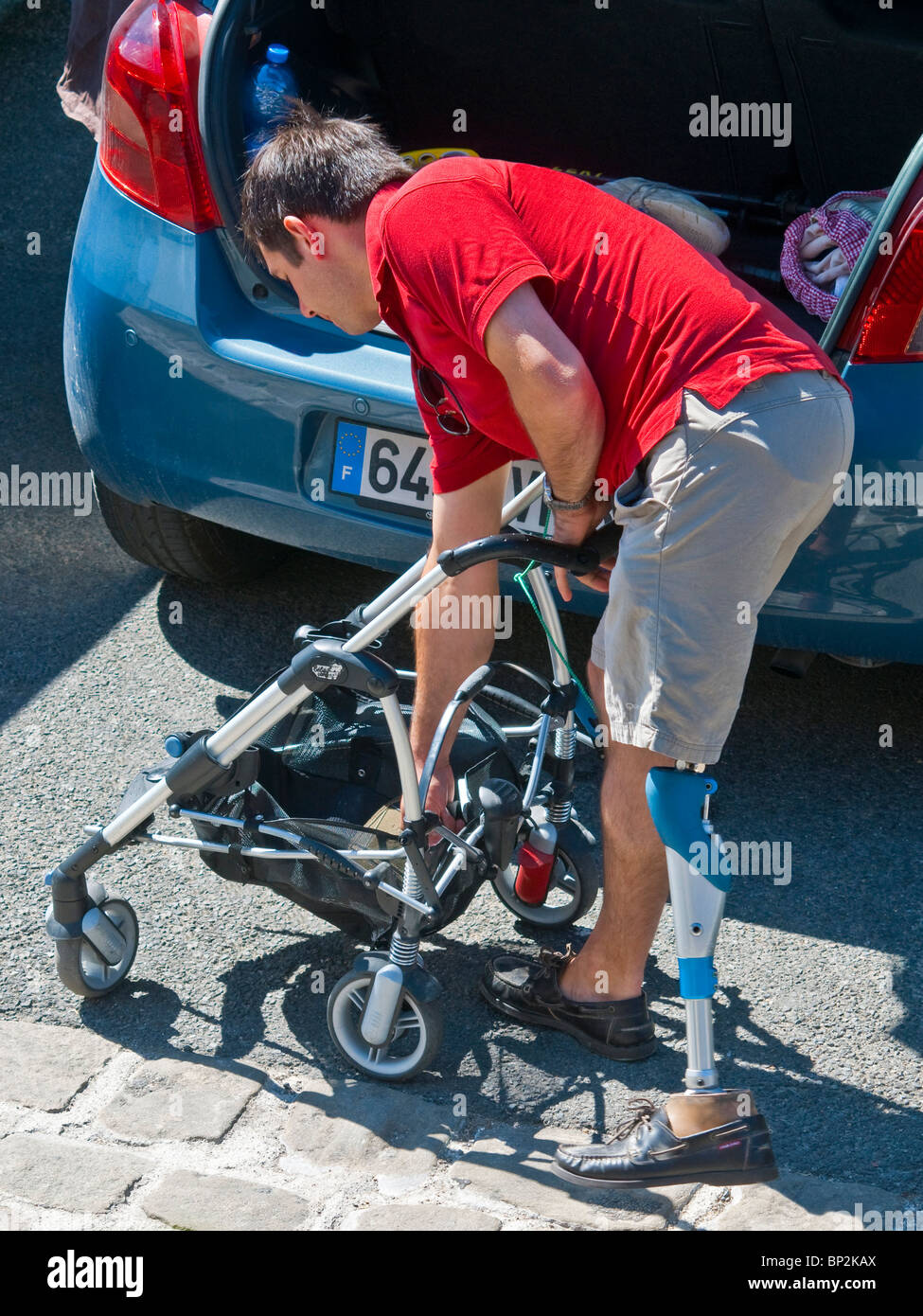 Mann mit Beinprothese laden Baby Wagen in Fließheck Auto - Frankreich. Stockfoto