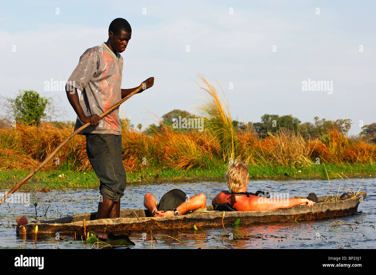Poler mit Touristen in einem Tradiional Mokoro Einbäume auf Exkursion in das Okavango Delta, Botswana Stockfoto