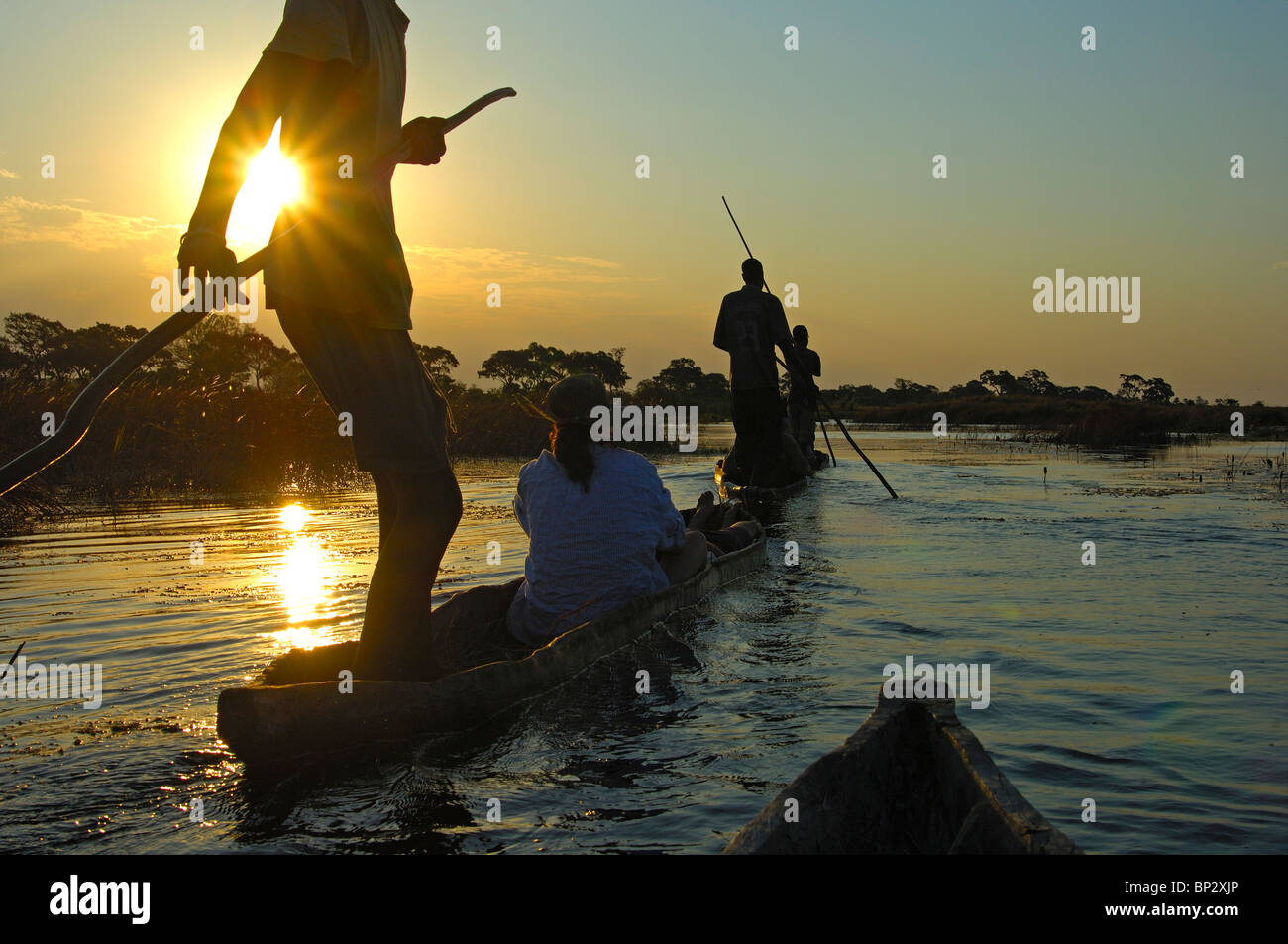 Schiffer mit Touristen im Mokoro Einbäume auf einen Sonnenuntergang Ausflug in das Okavango Delta, Botswana Stockfoto
