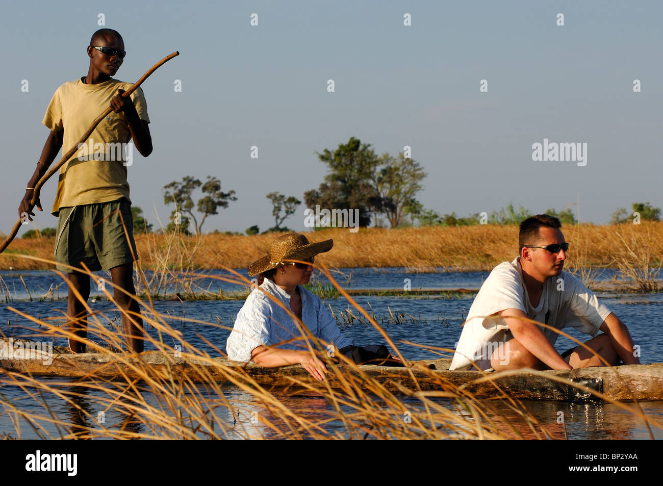 Poler mit Touristen in einem Tradiional Mokoro Einbäume auf Exkursion in das Okavango Delta, Botswana Stockfoto
