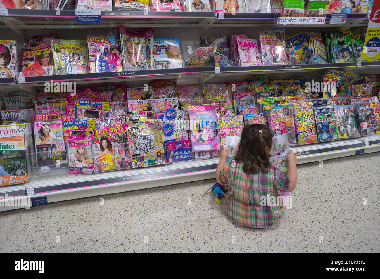 Das Überleben der gedruckten Seite - ein kleines Mädchen blättert die Kinder Comic-Zeitschriften in einem Zweig der Tesco in Schottland - Großbritannien Stockfoto