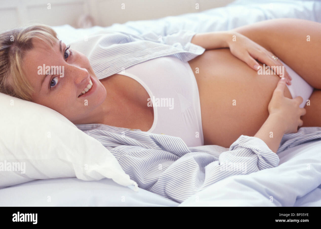 Schwangere Frau liegend auf einem Bett Bauch halten und Lächeln in die Kamera Stockfoto