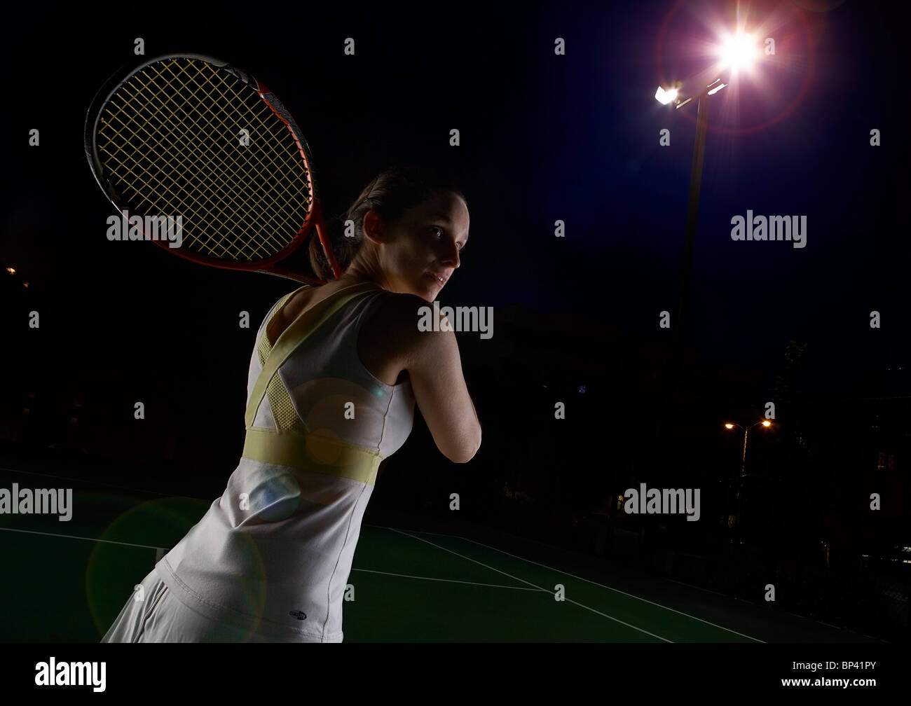 Eine Frau, die Tennis spielen in der Nacht auf einer Flut beleuchteten Tennisplatz Stockfoto