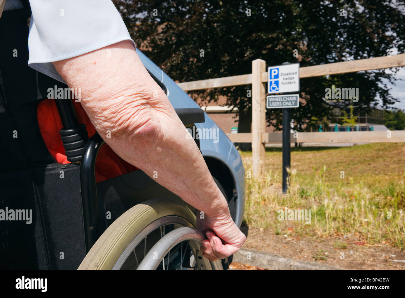 Ältere Frau in einem Rollstuhl von einem Auto in blue-Badge deaktiviert Parkplatz mit Zeichen für Rollstuhlfahrer nur geparkt. VEREINIGTES KÖNIGREICH. Stockfoto