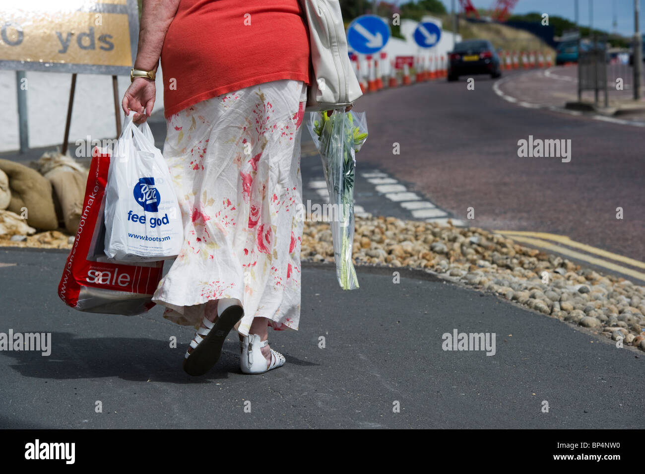 Eine Frau trägt ihr Einkaufen in Tragetaschen Spaziergänge entlang einer Brighton-Pflaster. Stockfoto
