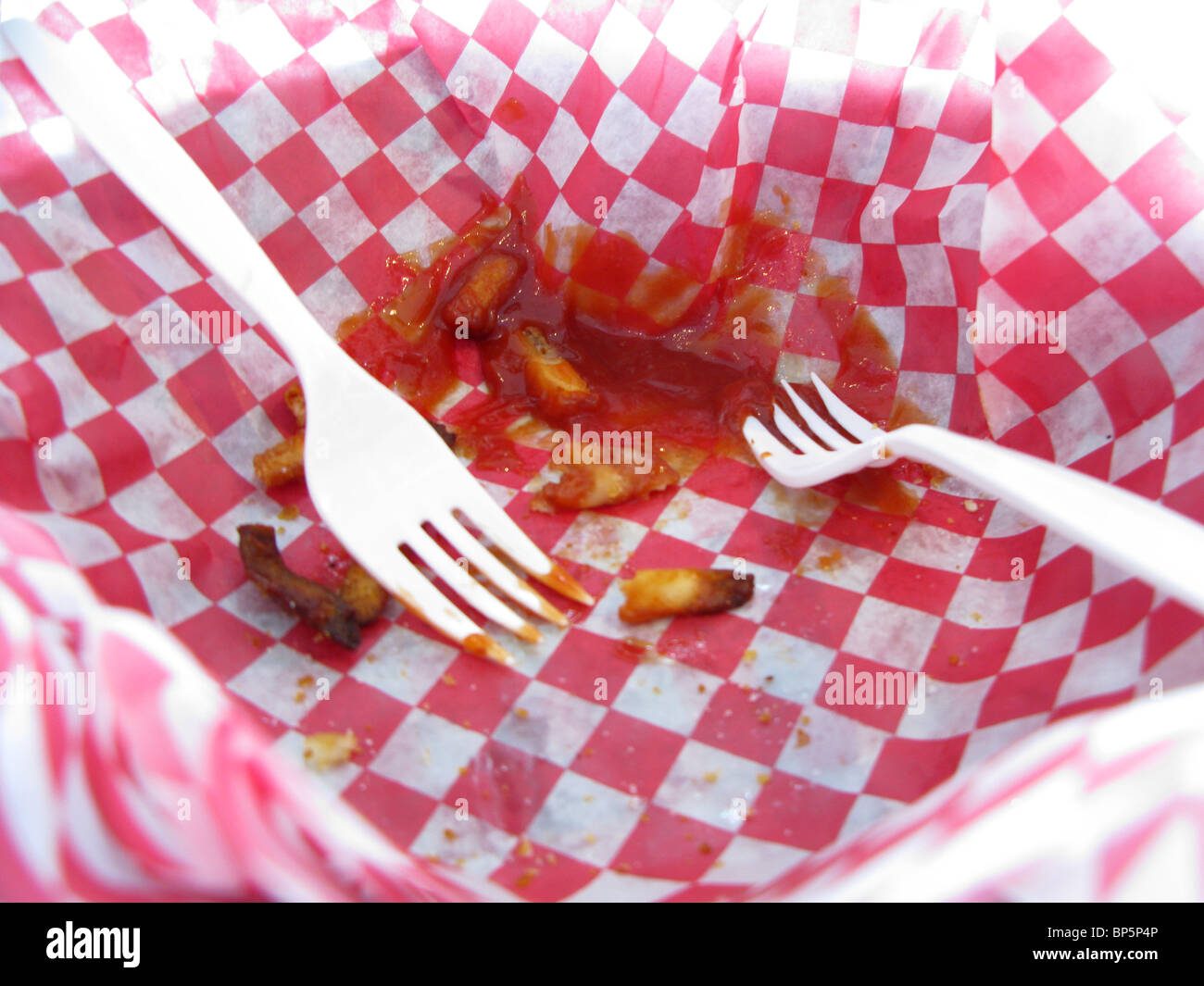 Zwei weiße Kunststoff Gabeln in einem rot-weiß karierten Korb mit Pommes und Ketchup gegessen Resten. Stockfoto