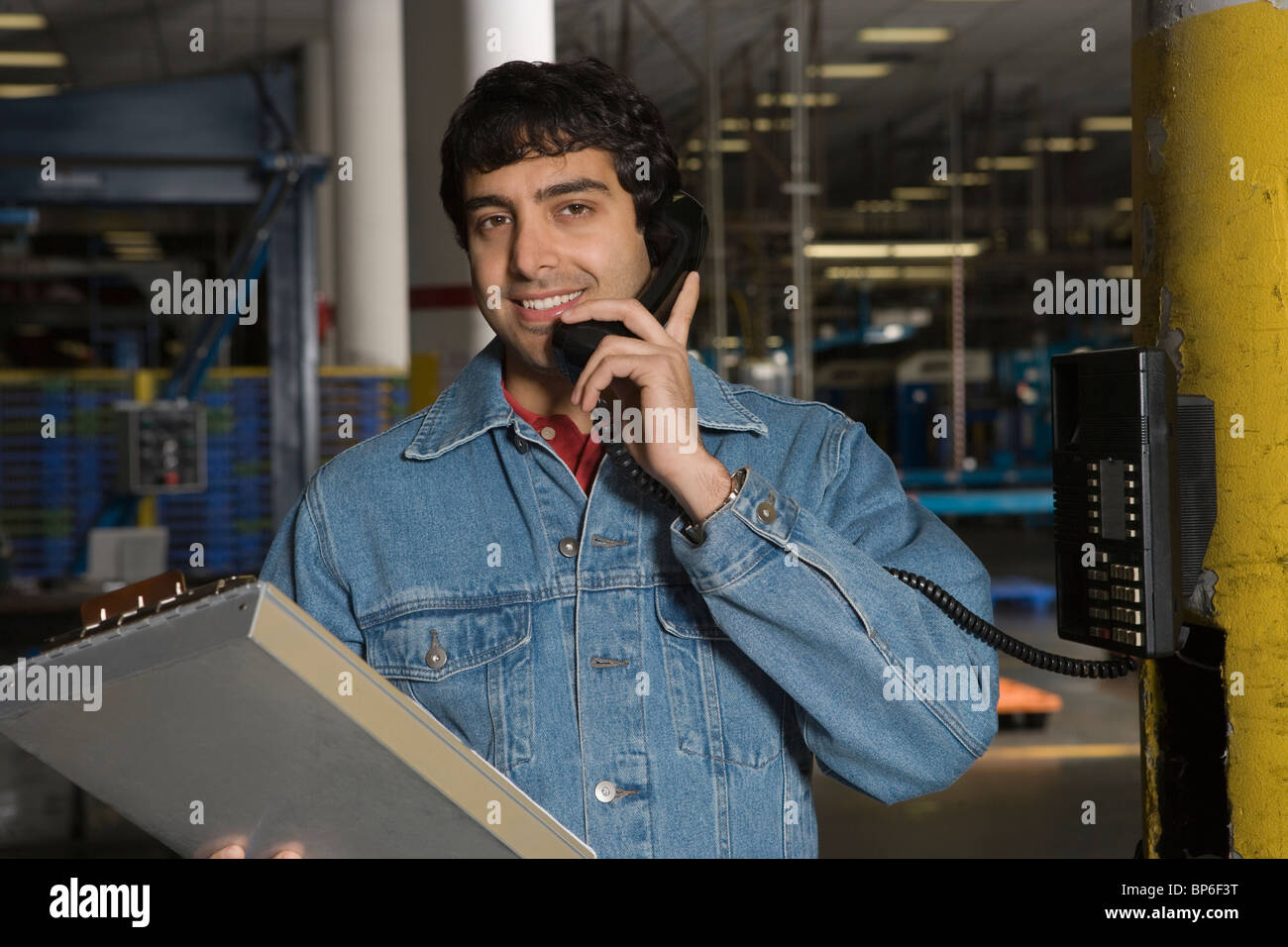 Fröhlicher Mensch mit Telefon in Fabrik Stockfoto