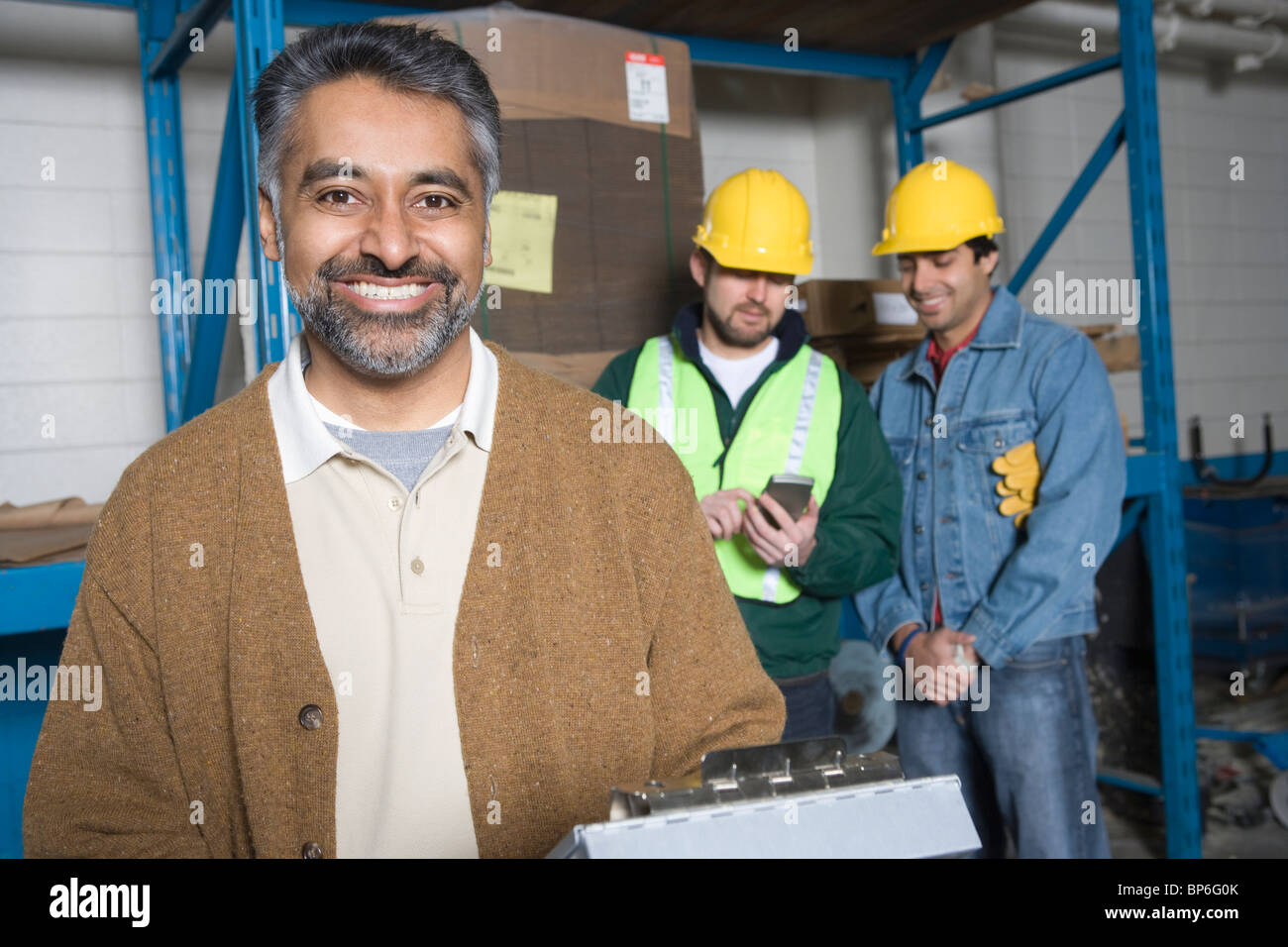 Fröhliche Männer in Fabrik, Kolleginnen und Kollegen im Hintergrund Stockfoto