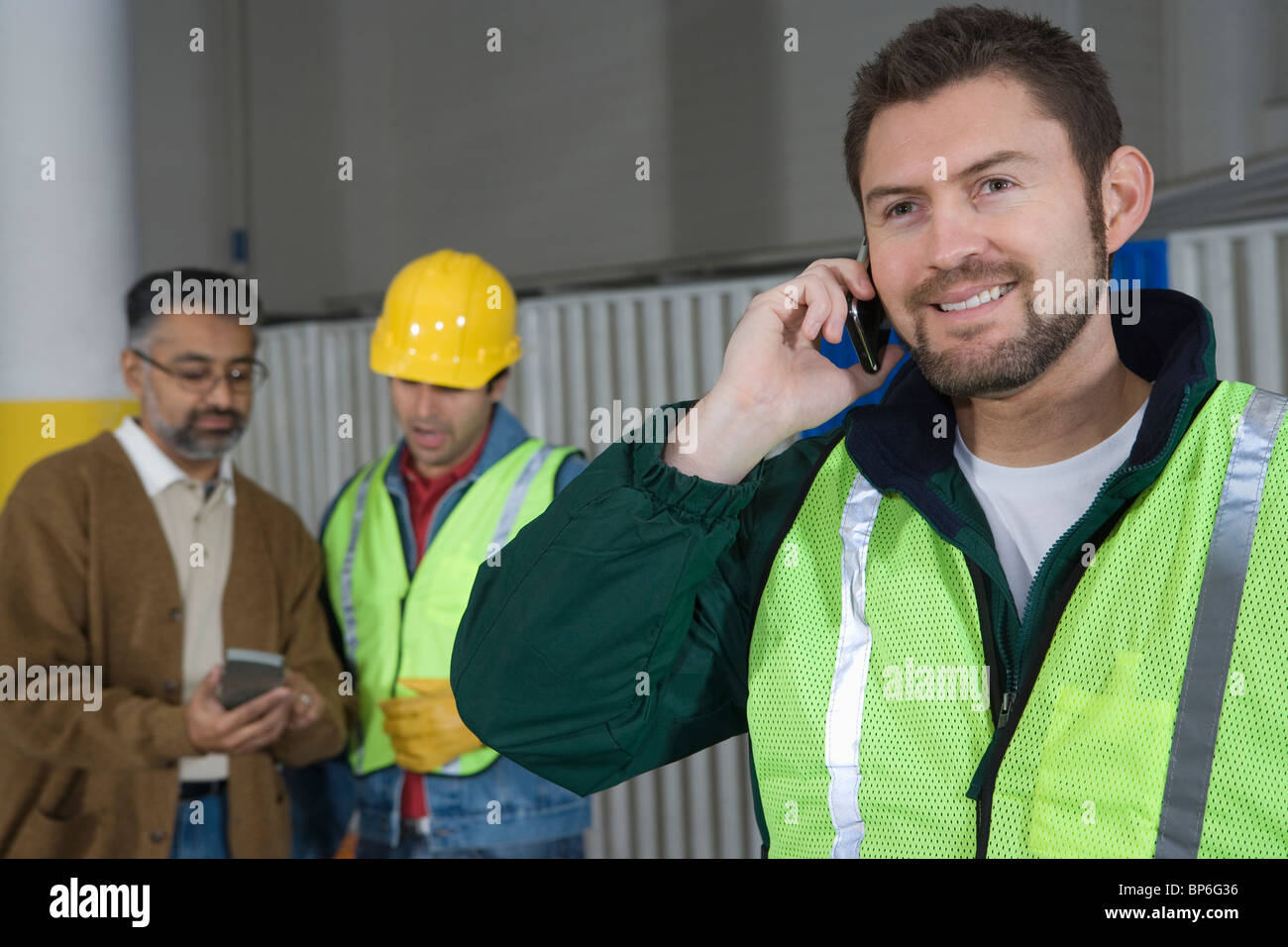 Mann stehend in Fabrik, mit Telefon, Kolleginnen und Kollegen im Hintergrund Stockfoto