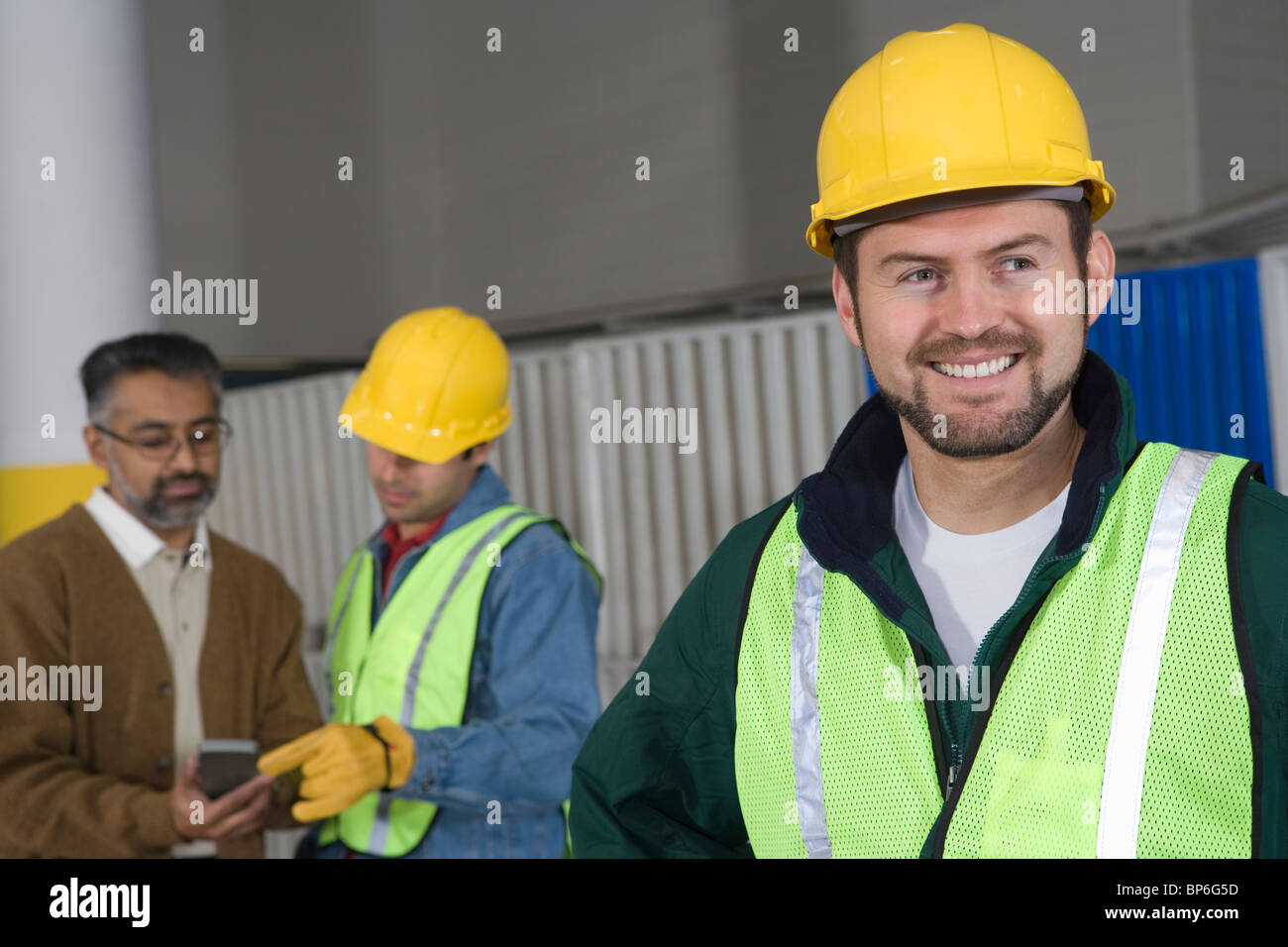 Fröhlicher Mensch stehen in Fabrik, Kolleginnen und Kollegen im Hintergrund Stockfoto