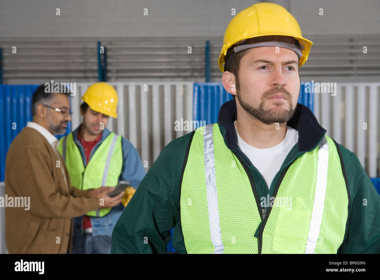 Ernster Mann stehend in Fabrik, Kolleginnen und Kollegen im Hintergrund Stockfoto